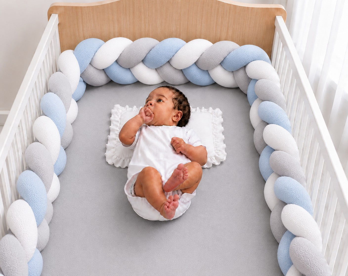 Tour de lit tressé bleu blanc et gris installé dans un berceau avec un bébé