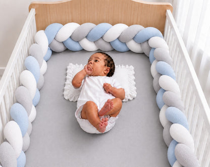 Tour de lit tressé bleu blanc et gris installé dans un berceau avec un bébé