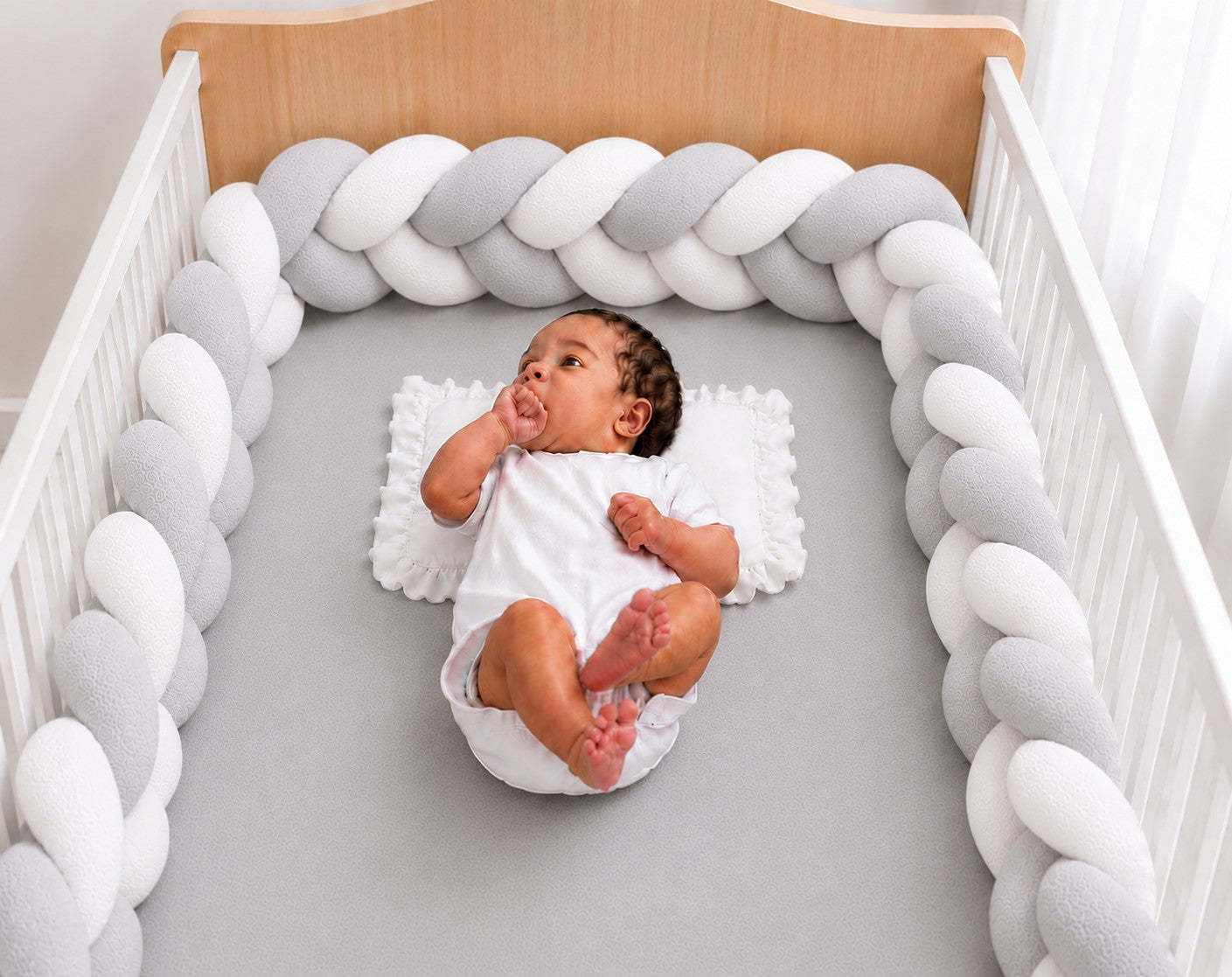 Tour de lit tressé gris et blanc installé dans un berceau avec un bébé