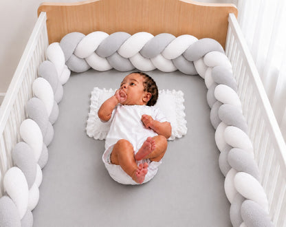 Tour de lit tressé gris et blanc installé dans un berceau avec un bébé