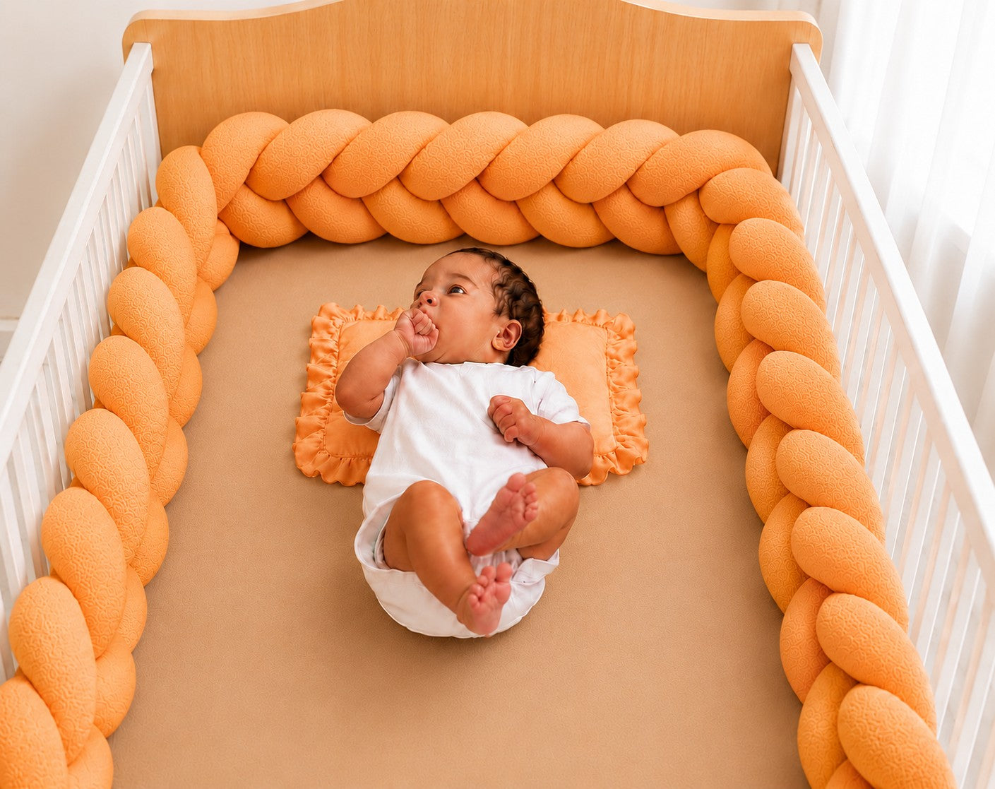 Tour de lit tressé orange installé dans un berceau avec un bébé