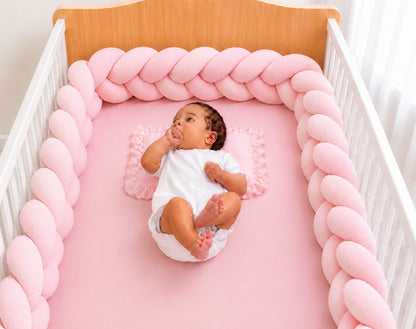 Tour de lit tressé rose installé dans un berceau avec un bébé