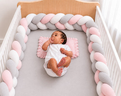 Tour de lit tressé rose blanc et gris installé dans un berceau avec un bébé