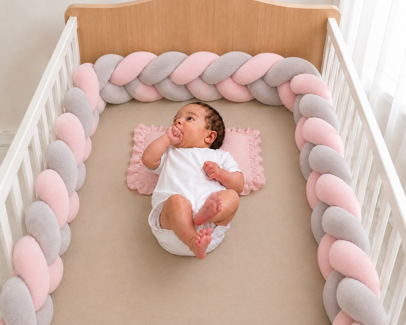Tour de lit tressé rose et gris installé dans un lit bébé