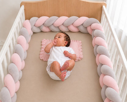 Tour de lit tressé rose et gris installé dans un lit bébé