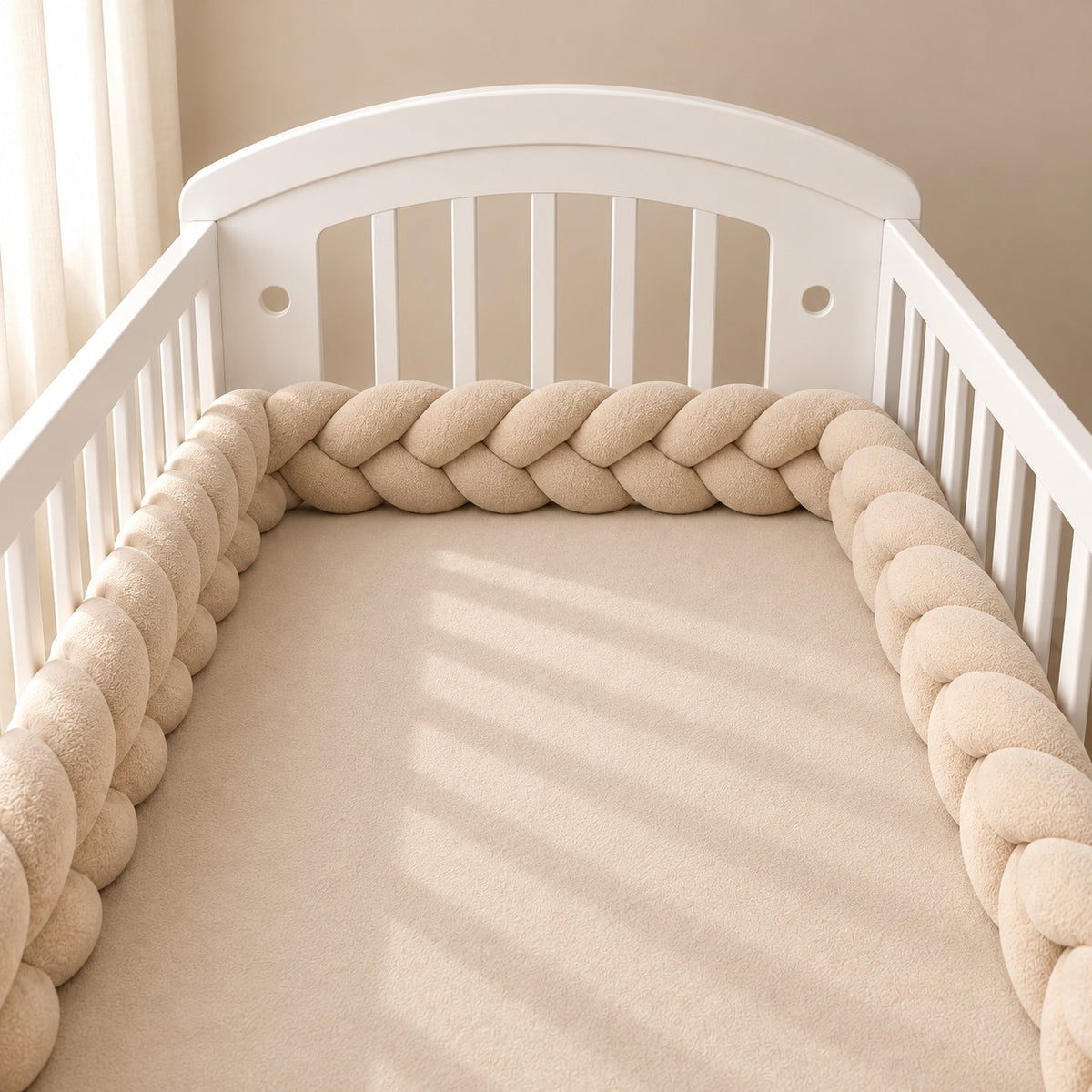 Tour de lit tressé beige installé autour du matelas d’un lit bébé blanc à barreaux
