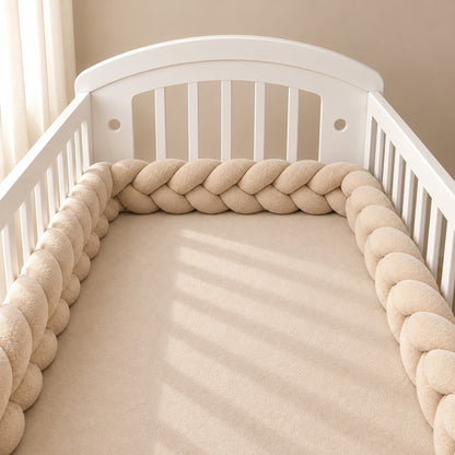 Tour de lit tressé beige installé autour du matelas d’un lit bébé blanc à barreaux
