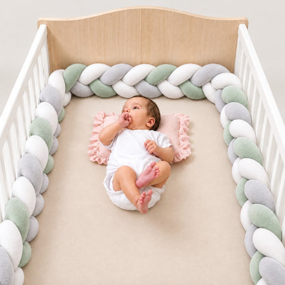 Tour de lit tressé blanc, vert sauge et gris installé autour d’un bébé dans un lit à barreaux blanc