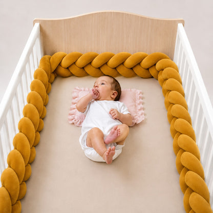 Tour de lit tressé jaune moutarde en tissu effet velours installé dans un lit bébé en bois.